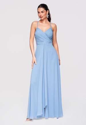 Kobieta w jasnoniebieskiej, długiej do ziemi sukni z cienkimi ramiączkami i marszczonym gorsetem, nosząca efektowne kolczyki, stojąca na jednolitym tle.