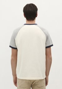 Chemise à manches courtes avec un corps crème, des manches raglan grises et un col marine. Texture lisse, coupe décontractée et sans motifs visibles.