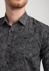 La camicia nera con bottoni presenta un motivo geometrico di linee e forme bianche, con un tessuto testurizzato e un design del colletto standard.