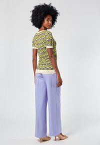 Top de punto de manga corta en patrón de olas amarillas y verdes, combinado con pantalones de pierna ancha en púrpura claro y tacones beige. Detalle de tejido texturizado.