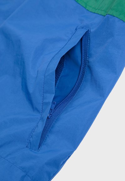 Blauwe buitenkleding met groene accenten, heeft een ritszak met een gaasinterieur, gemaakt van lichte, gestructureerde stof.