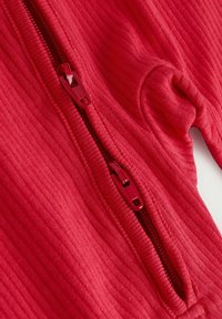 Rød ribbet stof zip-up top med dobbelt lynlås og tætsiddende design. Tekstureret overflade med synlige sømdetaljer.