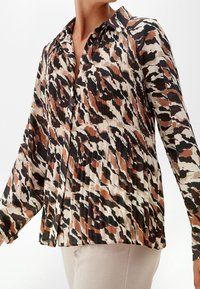 Camicia a maniche lunghe in tessuto leggero con un motivo astratto marrone e nero, chiusura con bottone e design plissettato.