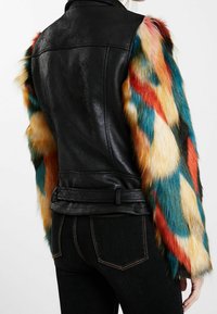 Czarna skórzana kurtka z wielokolorowymi rękawami z futerka ekologicznego, o gładkiej fakturze i abstrakcyjnych wzorach w kolorach czerwonym, niebieskim i żółtym.