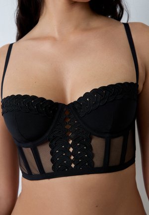 Reggiseno nero con un design strutturato, pannello in rete, bordo decorativo intrecciato lungo la parte superiore e spalline regolabili.