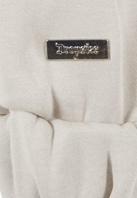 Hellgrauer Stoff mit weicher Textur, versehen mit einem geprägt metallischen Etikett, auf dem das Wort "Dropsie" steht. Der Stoff hat ein gerafftes Design.