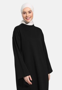 Black long-sleeve dress with a loose fit and round neckline. A light-colored hijab complements the outfit, adding a contrasting texture.