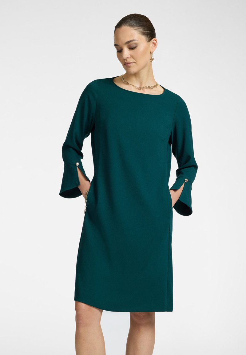 Teealfarbenes Kleid mit rundem Ausschnitt, dreiviertellangen Ärmeln mit Schlitzen und Knöpfen sowie seitlichen Taschen; glattes Material und bequemer Schnitt.
