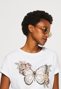 White short-sleeve t-shirt featuring a large butterfly graphic with floral accents in pink and green. Smooth cotton texture.
