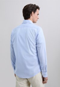 Camisa de rayas azul claro de manga larga con cuello clásico, puños con botones y dobladillo curvado. Tejido de algodón con una textura suave.