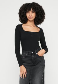 Zwart bodysuit met lange mouwen, een vierkante halslijn en een drieknops placket. Gecombineerd met een hoogtaillespijkerrok met klinknageldetail.