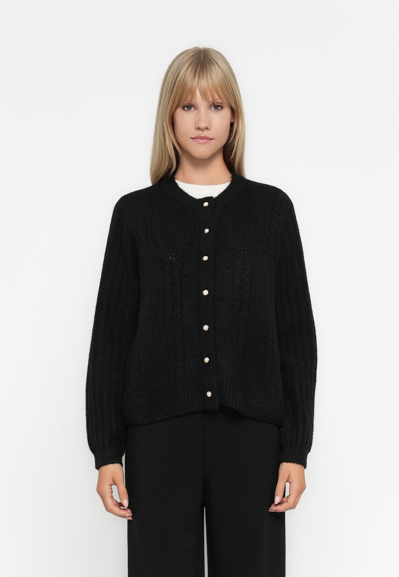 Cardigan en maille noire avec un motif texturé, col rond et boutons sur le devant. Manches longues avec poignets côtelés.