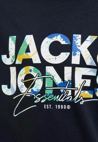 Mornarska majica s natpisom "JACK & JONES" velikim, podebljanim bijelim slovima uz šarene mrlje, te "Essentials EST. 1990" u rukopisnom fontu.