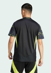 Schwarzes Sporttrikot mit kurzen Ärmeln, neongelben Akzenten an den Seiten und geometrischen Mustern auf den Schultern.