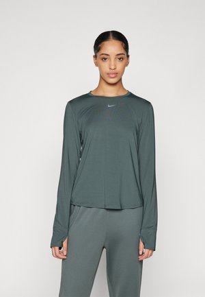 Langærmet træningstrøje i mørkegrønt stof. Har en rund halsudskæring og et subtilt Nike-logo mønster på brystet. Glat tekstur.