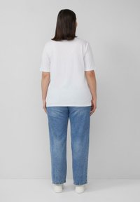 WitteT-shirt met korte mouwen en ronde hals, gecombineerd met lichtblauwe high-waisted jeans. De outfit wordt aangevuld met witte sneakers.