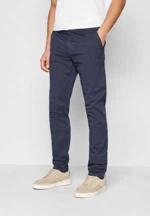 Chinos blu navy in un tessuto morbido e testurizzato con vestibilità slim, dotati di tasche laterali e una cintura liscia. Abbinati a sneakers beige.