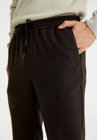 Bruine patroonde broek met een trekkoord in de taille, zijzakken en een gestructureerde stof, die een geruit ontwerp en neutrale kleurnuances laat zien.