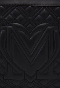 Černá kožená taška s prošívaným designem, výrazným embosovaným logem a kontrastním prošíváním. Hladký povrch s geometrickým vzorem.