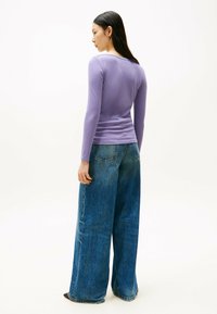 Lila Langarm-Rippoberteil kombiniert mit locker sitzenden, hoch taillierten blauen Denim-Jeans. Strukturiert, weit geschnitten und mit minimalen Details.
