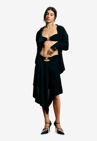 Mustast kahest osast koosnev komplekt, mis sisaldab metallaksendiga bandeau-tüüpi topi, voolavat asümmeetrist seelikut ja musti kõrge kontsaga kingi.