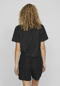 Čierne bavlnené tričko s krátkymi rukávmi, voľný strih, zlúčené s čiernymi šortkami. Hladká textúra, jednoduchý dizajn, žiadne viditeľné vzory ani kovania.