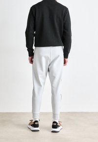 Schwarzer Sweatshirt und hellgraue Jogginghose mit schwarzen Seitenstreifen, ergänzt durch schwarze und braune Sneakers mit weißen Sohlen.