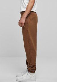 Bruine sweatpants van een zacht materiaal, met een elastische tailleband en omgeklepte enkels, gecombineerd met witte sneakers.