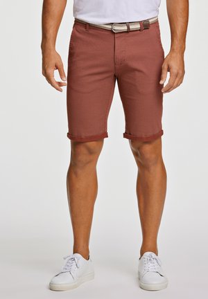 Shorts marron à motif avec des ourlets retroussés, associés à une ceinture tissée et des baskets blanches. Le tissu a une finition texturée.