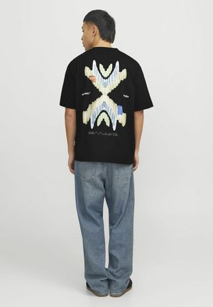 Sort kortærmet t-shirt med et farverigt abstrakt design på ryggen, parret med lyseblå løse jeans.