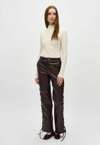 Crèmekleurig, textuur long-sleeve top gecombineerd met strakke bruin leren broeken met zijlacing en metalen oogjes. Bessenrode instappers maken de outfit af.