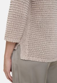 Gebreide trui in lichtbeige met een gestructureerd patroon, cropped mouwen en zijsplitten, gecombineerd met een gladde, olijfgroene broek.