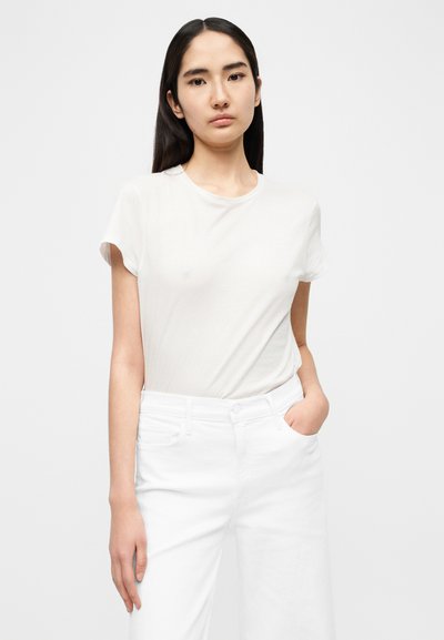 Ανοιχτό μπεζ μπλουζάκι με κοντά μανίκια, στρογγυλή λαιμόκοψη και απαλή υφή, σε συνδυασμό με λευκά ψηλόμεσα τζιν που διαθέτουν μπροστινές τσέπες.