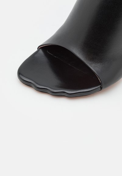 Czarne klapki odkryte palce z gładką skórzaną powierzchnią, z falistym brzegiem na cholewce oraz płaską podeszwą. Prosty i nowoczesny design.