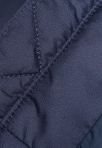 Tessuto trapuntato blu navy con una consistenza liscia, caratterizzato da motivi di cucitura diagonale e una leggera lucentezza. Motivo a griglia sottile visibile.