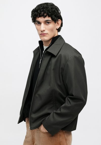 Donkergrijze ritsjack met een kraag en een gestructureerde stof, voorzien van twee zijzakken en een ingetogen ontwerp.