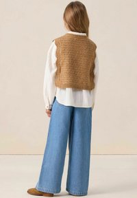 Gilet en tricot marron avec des bords festonnés, porté sur une chemise blanche à boutons. Jean large bleu clair, ample et léger. Tissu doux et texturé.