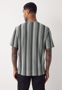 Kurzärmliges Hemd mit vertikalen schwarzen und grauen Streifen. Weiche Textur und lockere Passform, mit rundem Ausschnitt und leicht geschwungenem Saum.