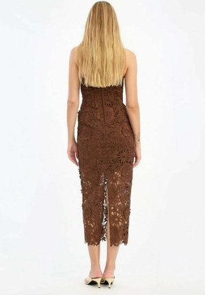 Donna con capelli biondi lunghi che indossa un abito midi marrone in pizzo floreale senza spalline e sandali chiari con tacco alto, vista da dietro.