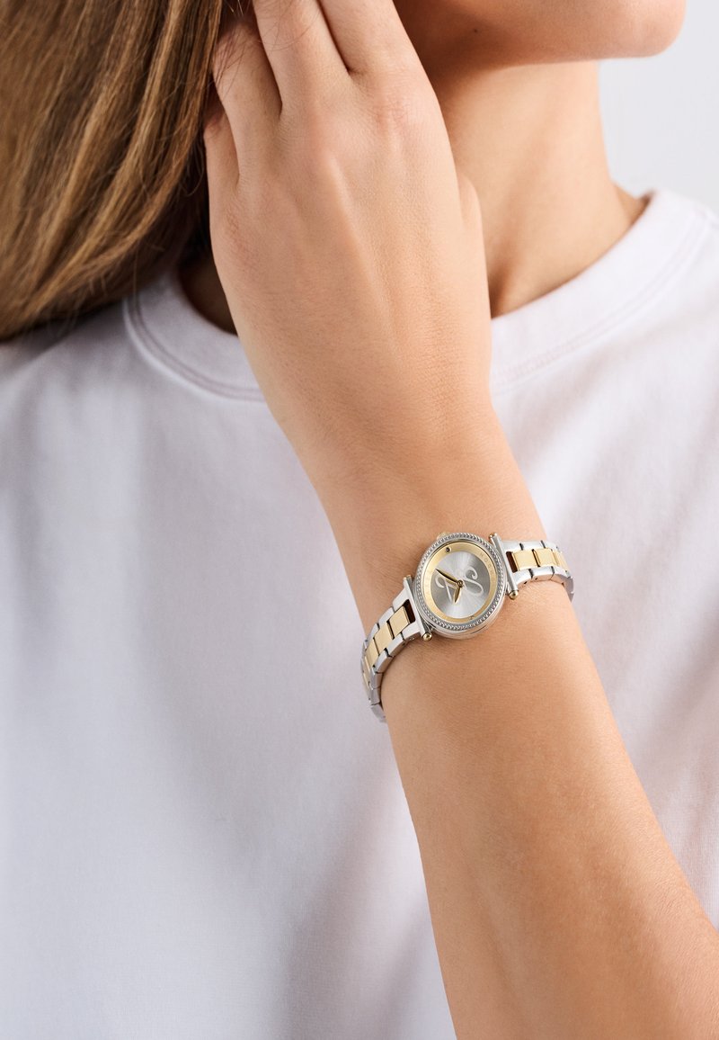 Zilveren en goudkleurige polshorloge met een ronde wijzerplaat, verhoogde bezel en schakelarmband. Heeft een minimalistische wijzerplaat met twee wijzers.