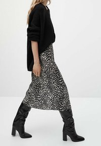 Pull noir oversize, jupe maxi à motifs avec des taches abstraites noires et blanches, et bottes noires montantes à talons blocs.