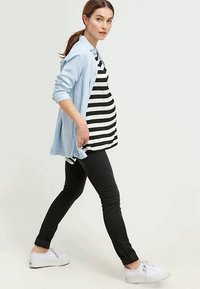 Conjunto de maternidade com um cardigan azul claro, jeans skinny pretos e uma camisola risca preta e branca; ténis brancos completam o visual.