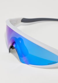 Sportsolglasögon med krökt blå gradientlins, vit ram och grå öronstöd; har UV-skydd och lätt design.