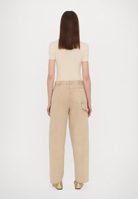 Beige ribbed short-sleeve top paired with loose, light beige pants featuring a back pocket and an adjustable waistband, worn with metallic loafers.