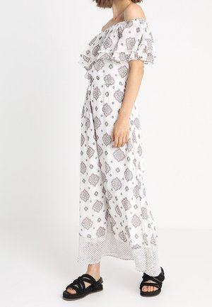 Off-shoulder maxi-jurk van lichtgewicht, witte stof met zwarte decoratieve patronen. Heeft gelaagde ruches mouwen en een stippenrand.
