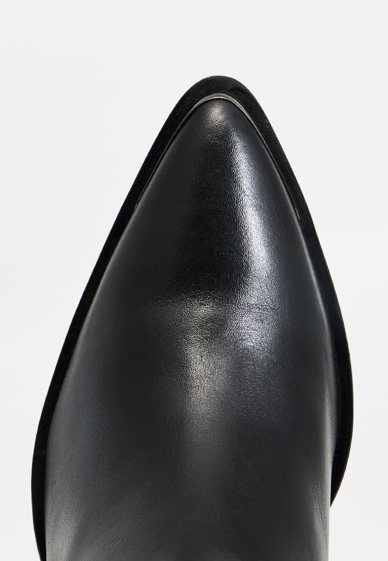 Czarne skórzane buty na szpilce o ostrej końcówce, z gładkim, błyszczącym wykończeniem i subtelnym metalicznym wykończeniem wzdłuż krawędzi podeszwy.