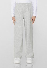 Šedé tepláky vyrobené z měkké tkaniny, s volným střihem a elastickým pasem. Spárované s bílými teniskami.