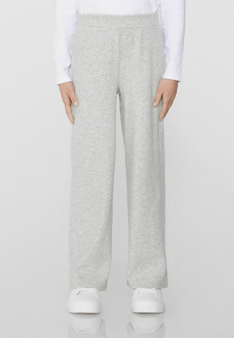 Šedé tepláky vyrobené z měkké tkaniny, s volným střihem a elastickým pasem. Spárované s bílými teniskami.