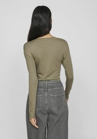 Khaki långärmad topp av slät tyg, kombinerad med högmidjade grå jeans med strukturerade sömmar och två bakfickor.