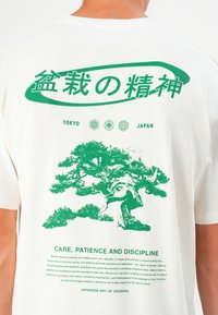White cotton t-shirt featuring a green bonsai tree graphic on the back with Japanese text, surrounded by circular symbols and text below.
